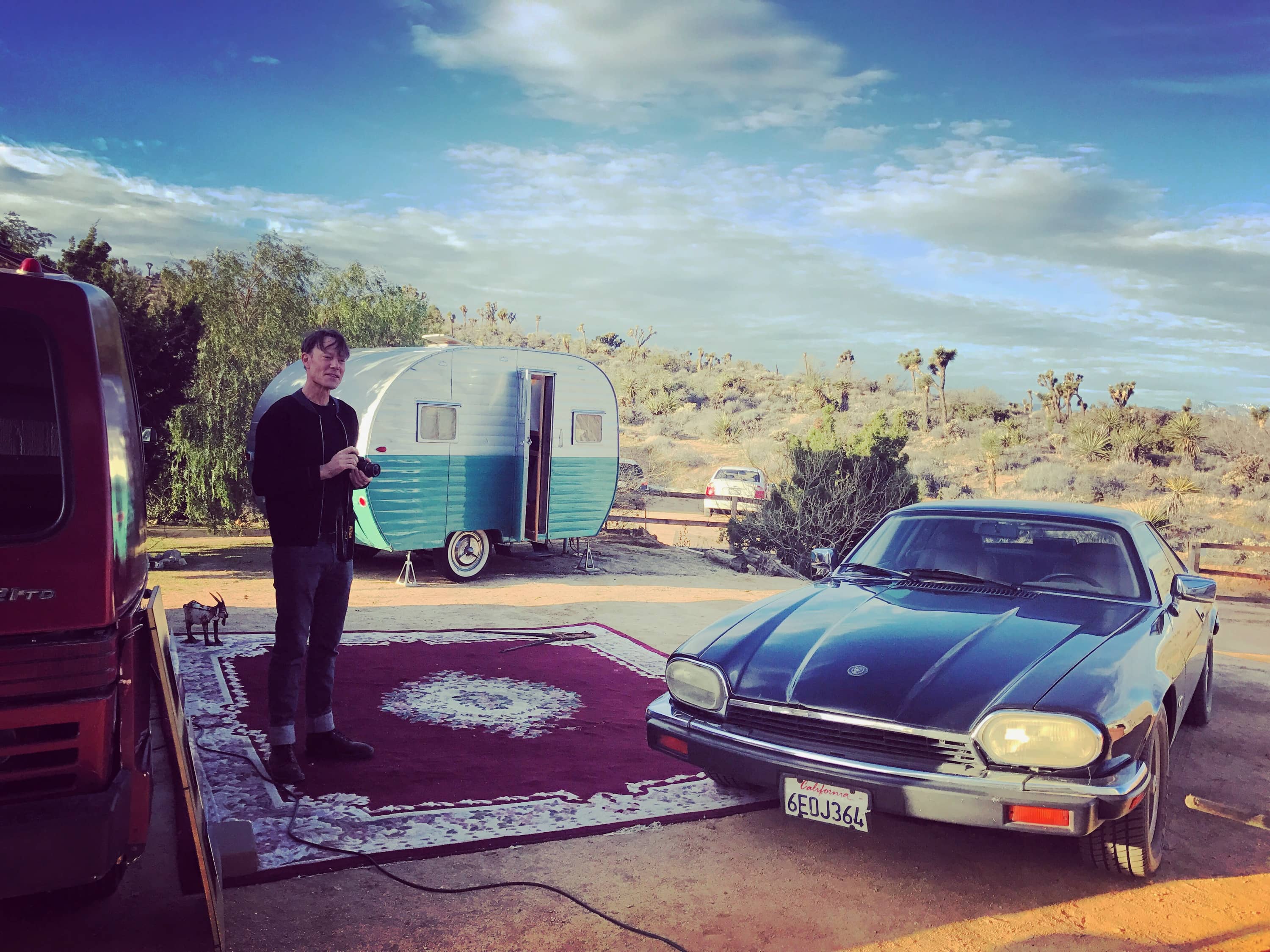 Andrew in the desert next to an old car in front of a trailer.